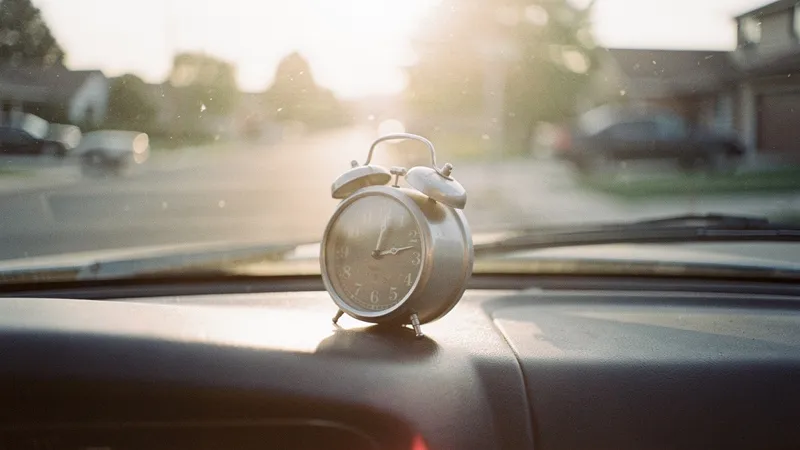 A small wind-up clock on a car dashboard at sunrise.
